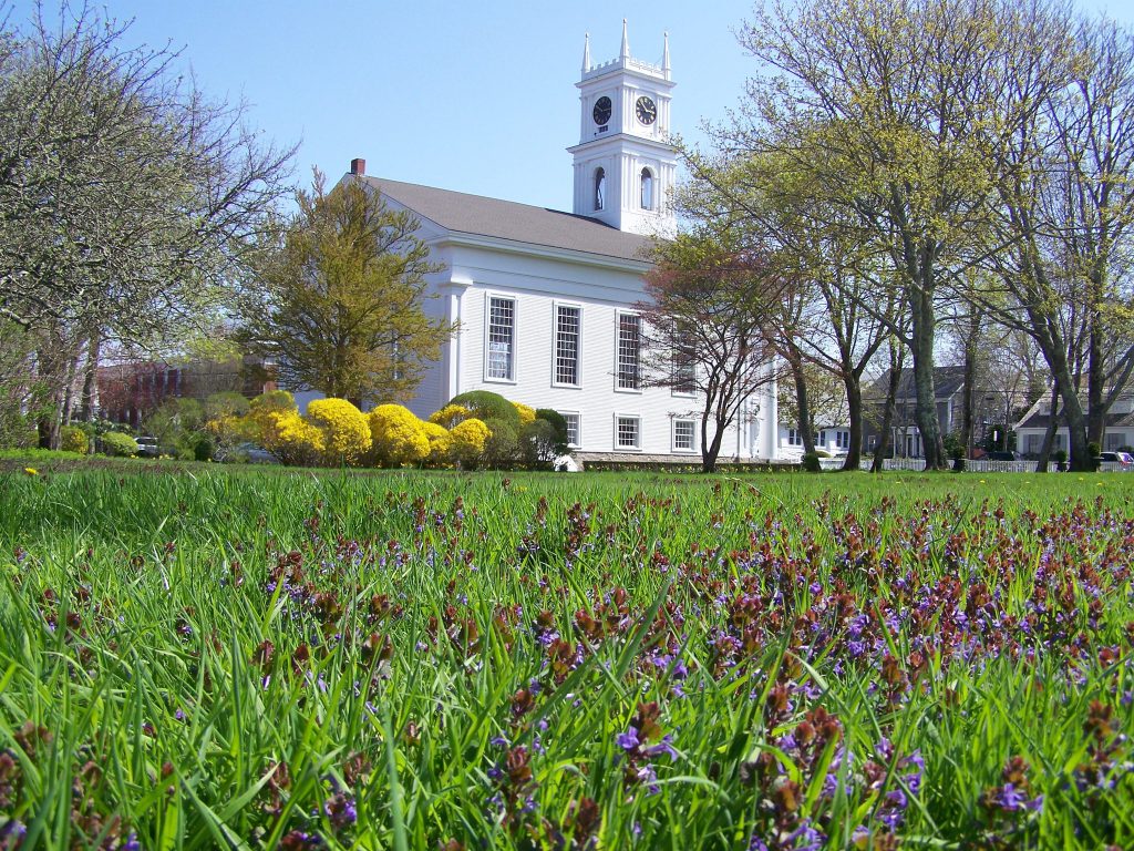 Seasonal Spring Re-Openings We're Excited For on Martha's Vineyard spring lawn with green grass and purple flowers with Old Whaling Church in the background