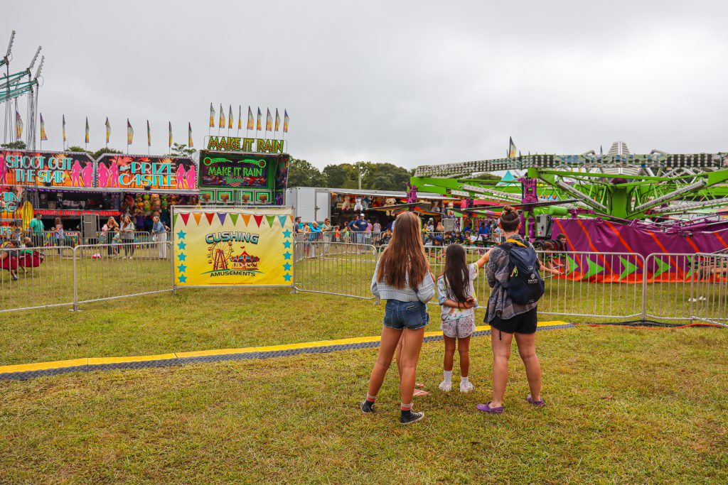 Three children standing in front of fair rides. 